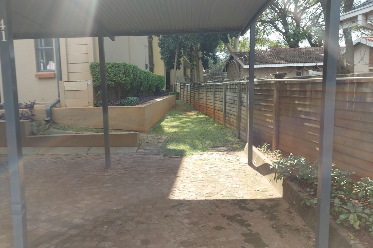 A rear exterior view featuring a covered carport, paved driveway, and a fenced boundary with a small garden area.