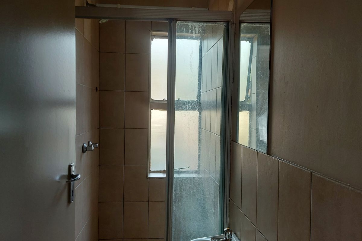 A compact bathroom featuring a shower enclosure with tiled walls and a fixed mirror, requiring cosmetic updates to improve its overall condition.