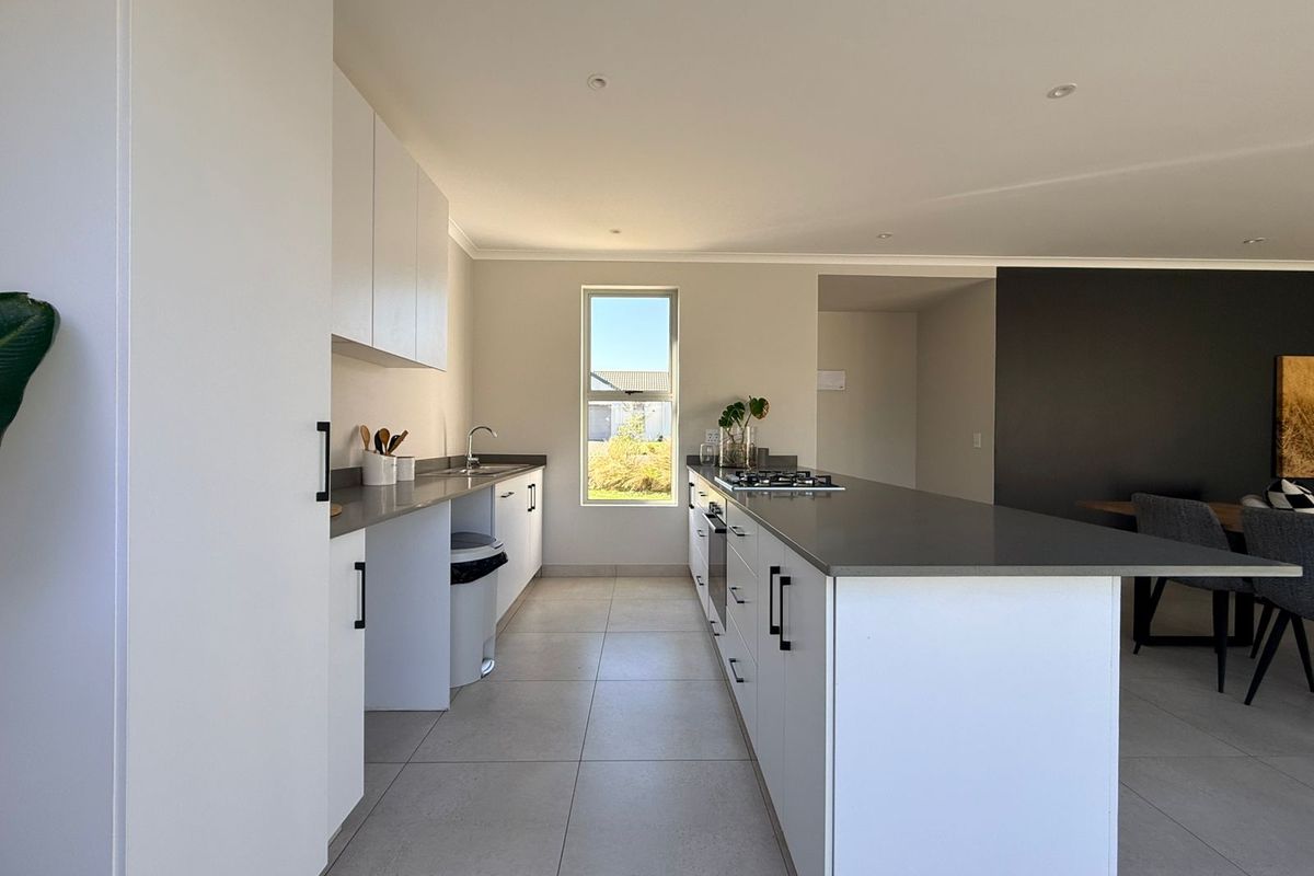 Modern kitchen featuring sleek white cabinetry, stone countertops, a central island with a gas hob, and high-quality tiled flooring.