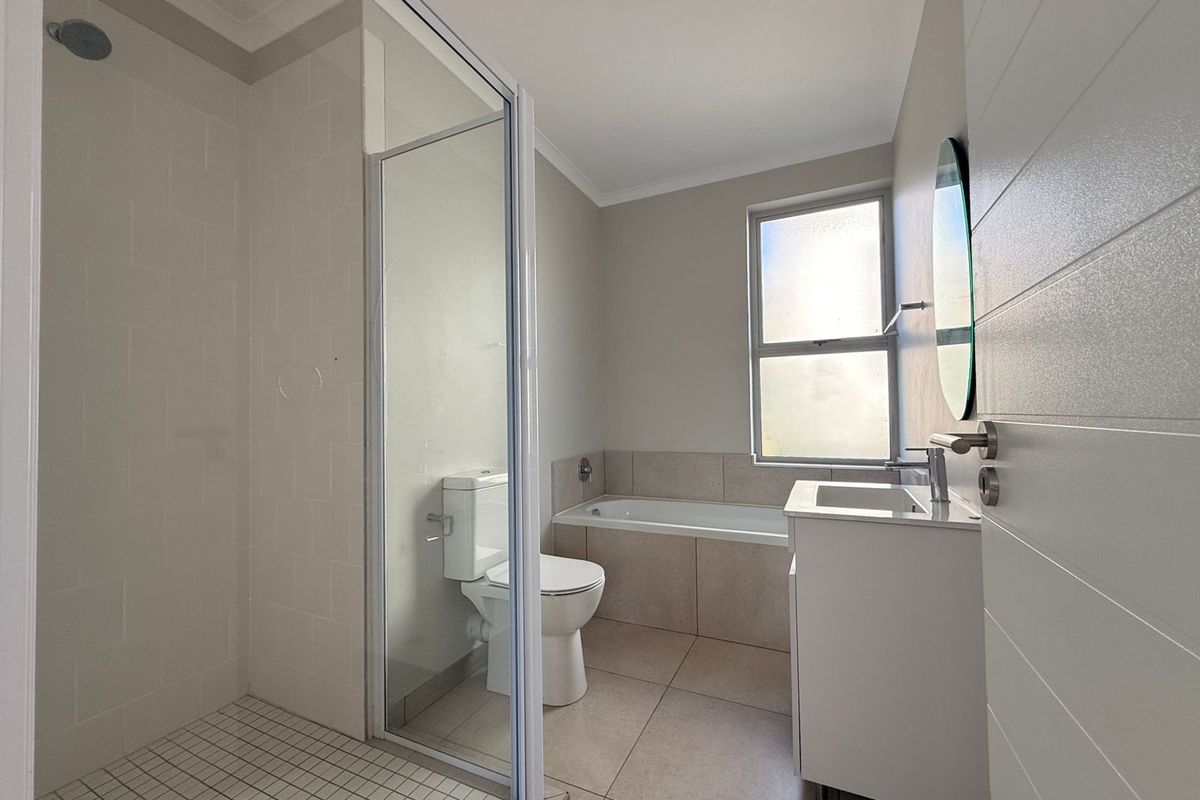A clean, modern bathroom featuring a walk-in shower with glass enclosure, a built-in bathtub, a vanity with basin, and neutral floor-to-ceiling tiling.