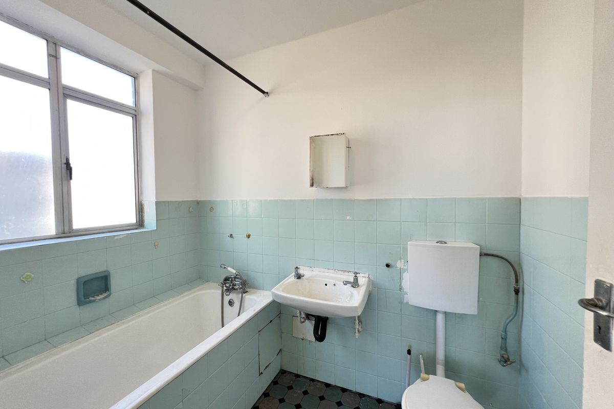 A dated bathroom featuring original light blue wall tiling, a standard bathtub, wall-mounted basin, and a high-level cistern toilet.