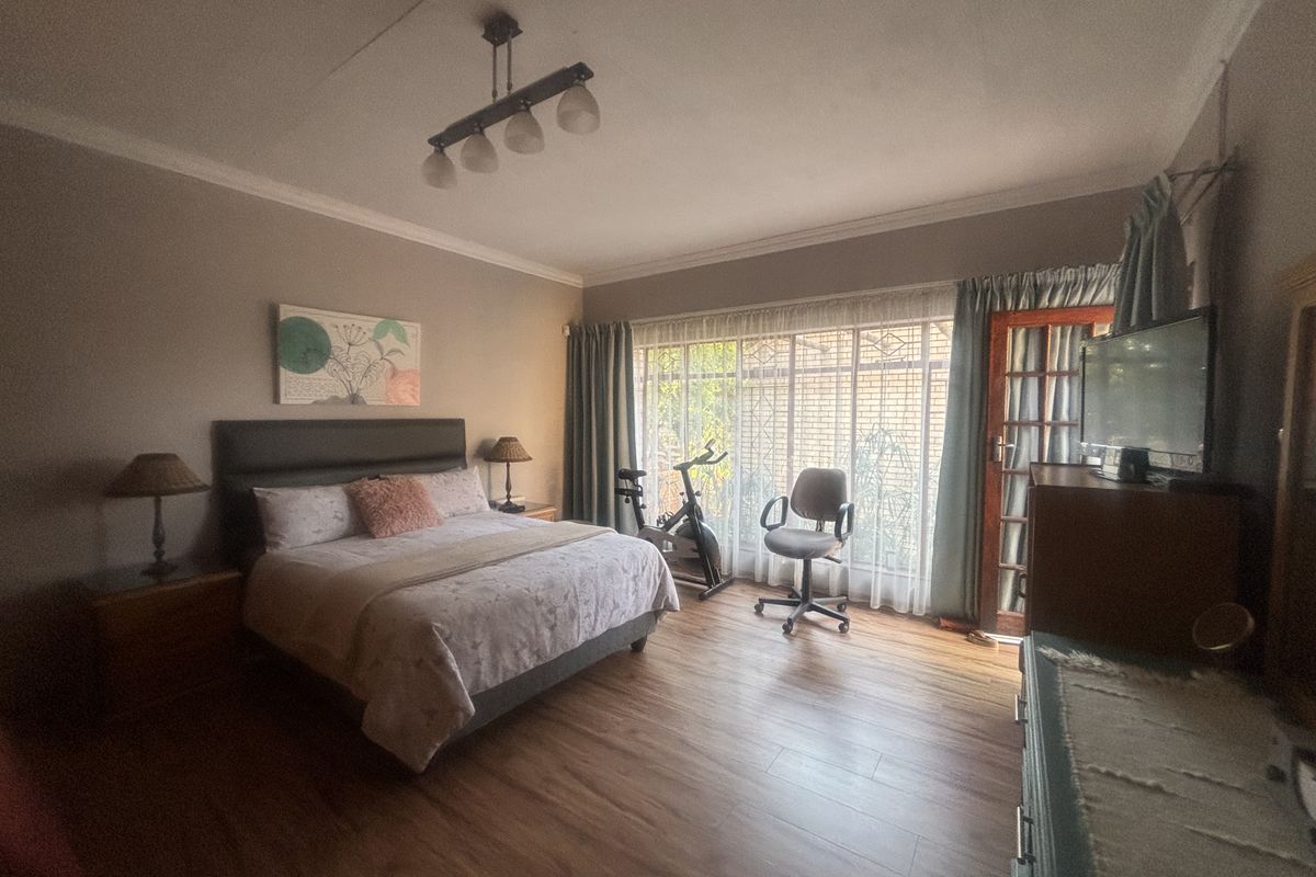 Spacious bedroom featuring laminate flooring, a ceiling light fixture, and direct access to the garden through a timber framed glass door with security gate.