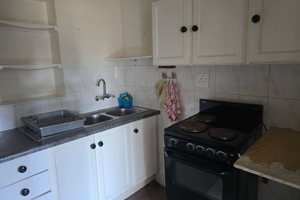 A compact kitchen featuring white cabinetry, a double bowl sink, tiled splashback, and a freestanding electric stove.