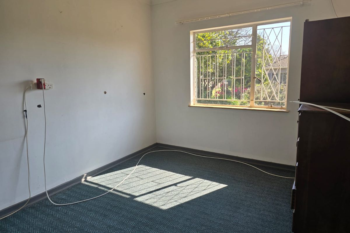 A vacant bedroom featuring carpet flooring, security bars on the window, and coving, requiring minor cosmetic updates to the wall surfaces.