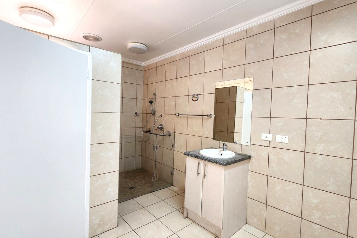 A functional bathroom featuring a walk-in shower with glass enclosure, a vanity unit with basin, and neutral wall tiling throughout.