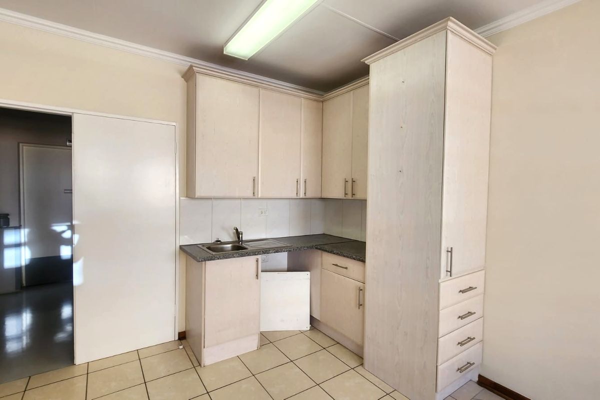 A compact kitchen area featuring light-toned laminate cabinetry, granite countertops, and tiled flooring, currently requiring minor repairs to the lower cabinetry.