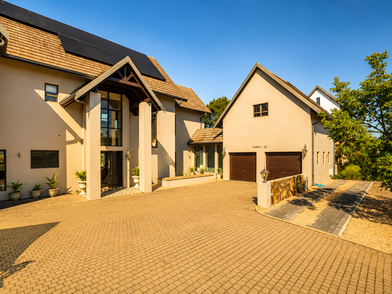 A well-maintained townhouse exterior featuring a paved driveway, double garage with timber doors, and modern architectural details including solar panels and stone accents.
