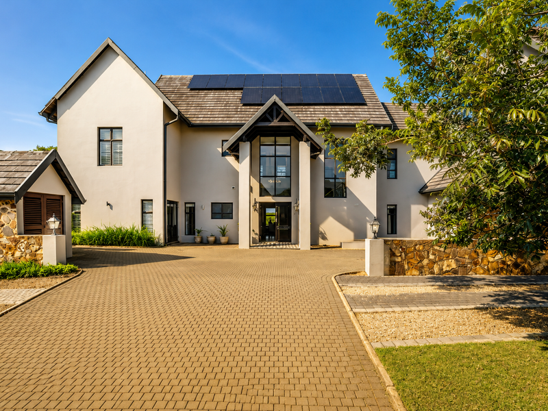 Impressive double-storey townhouse facade featuring stone cladding, a paved driveway, and integrated solar panels on the roof.