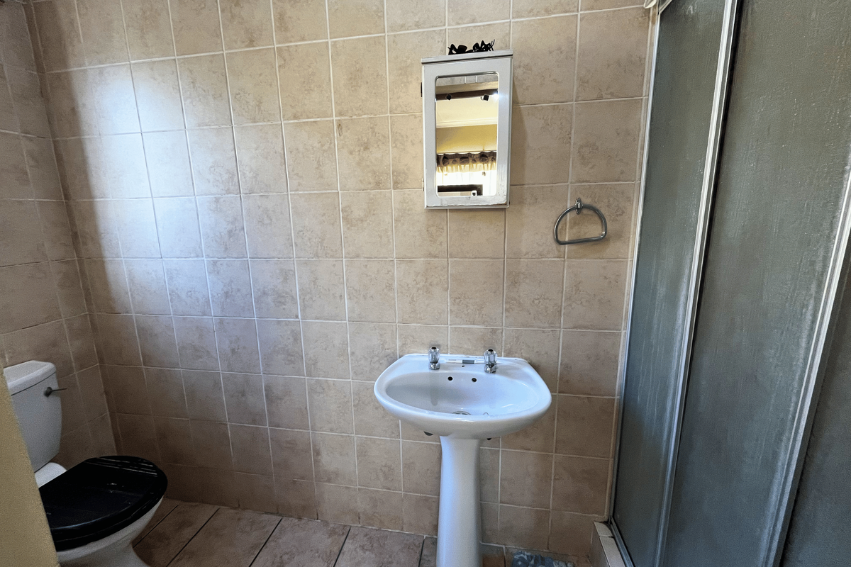 A dated bathroom featuring a pedestal basin, toilet, and a shower enclosure with tiled walls and flooring.