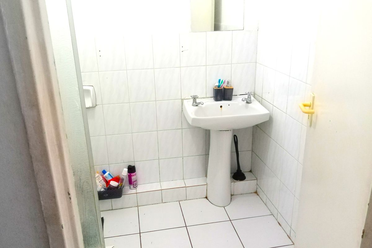 A compact bathroom featuring a pedestal basin, tiled surfaces, and a shower enclosure. The space requires cosmetic updates to improve its overall condition.