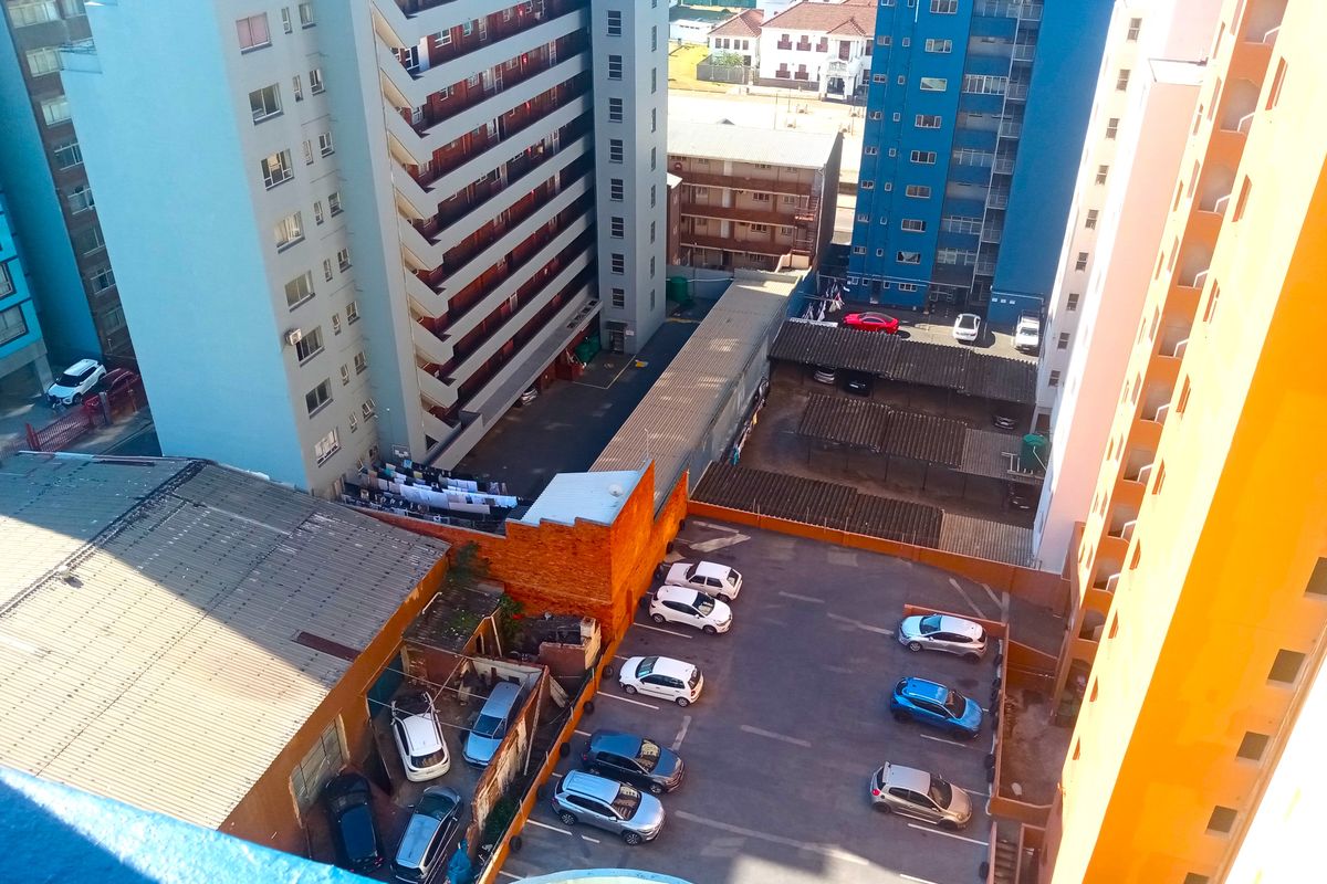 An elevated aerial view looking down onto a residential apartment complex parking area with multiple parking bays and surrounding building facades.