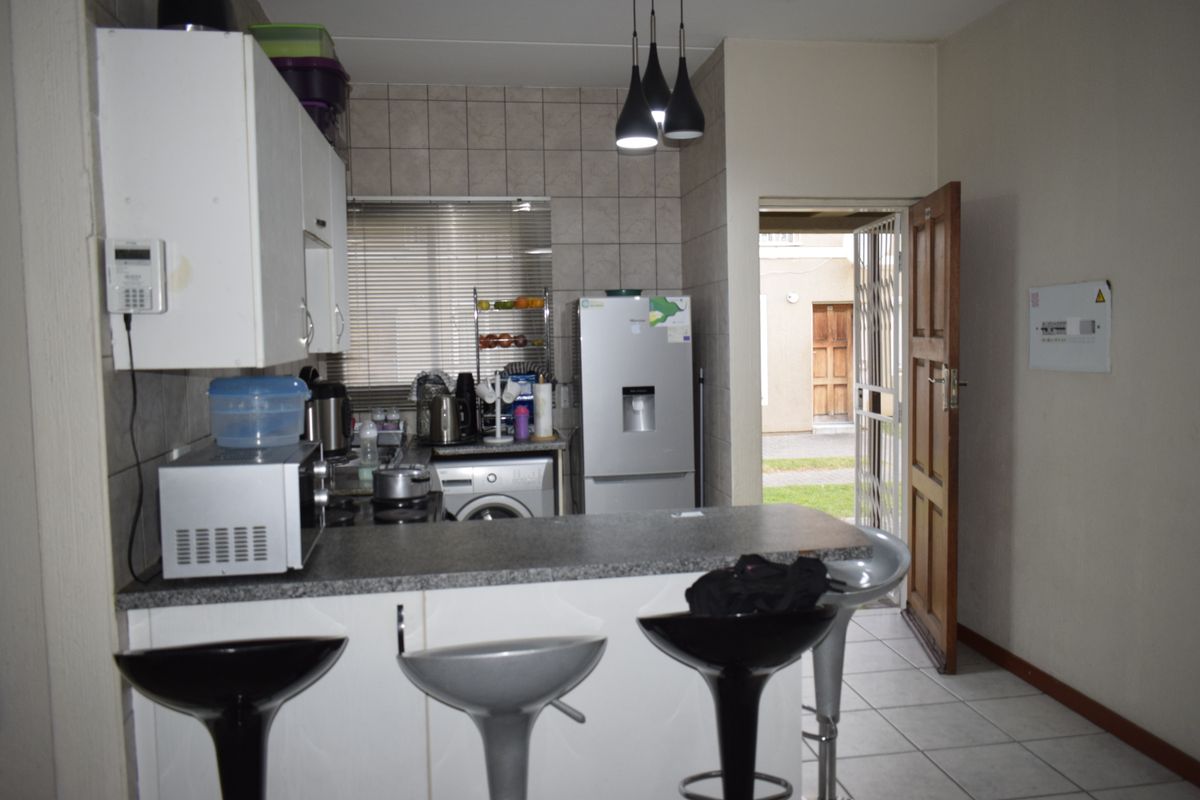 A functional kitchen featuring built-in cabinetry, a breakfast bar, tiled backsplash, and direct access to the exterior through a security gate.