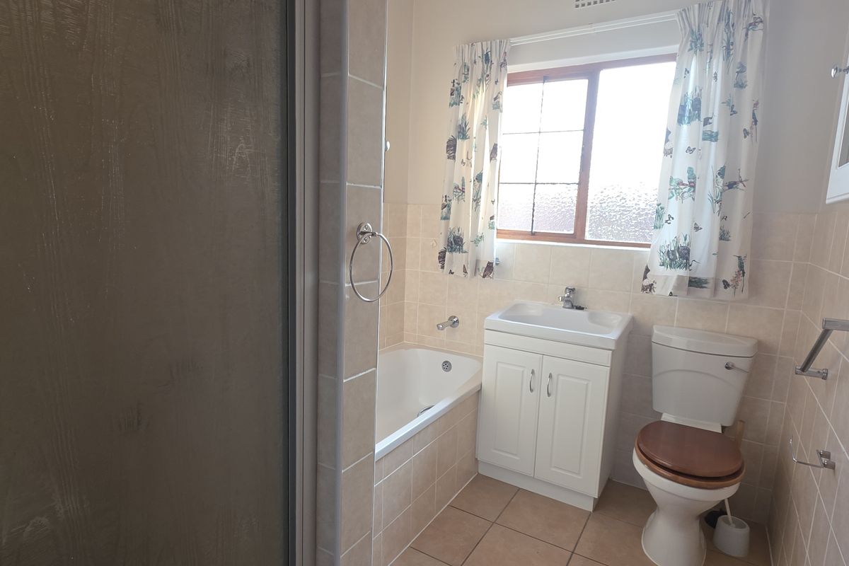 A functional bathroom featuring a built-in bathtub, vanity basin, and toilet with neutral wall tiling and a window for natural light.