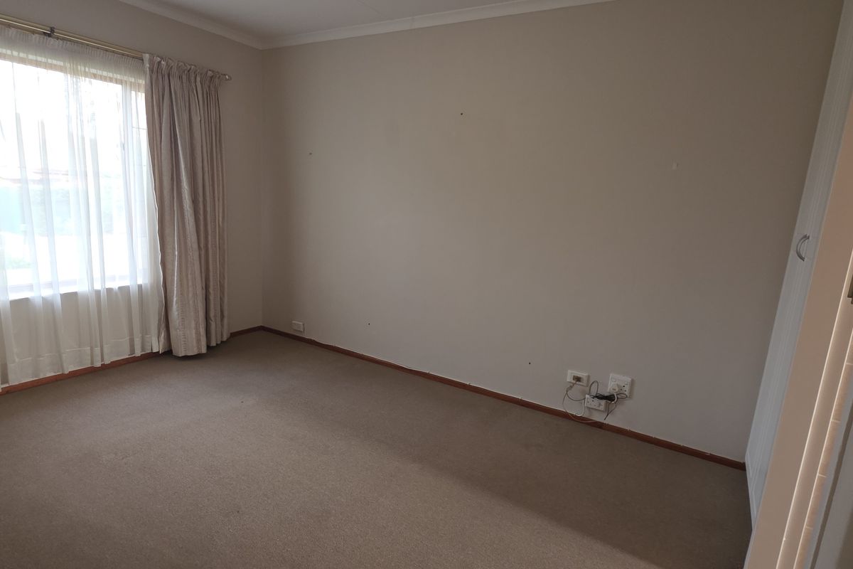 A vacant bedroom featuring neutral wall tones, carpeted flooring, and a large window with curtain tracks.