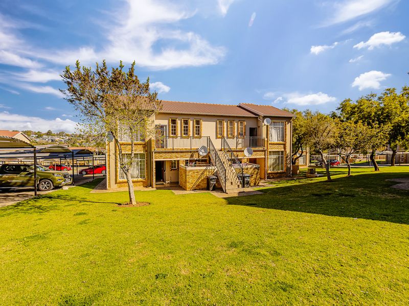 Rear view of a multi-story apartment complex featuring brick construction, an external staircase, and well-maintained communal garden areas.