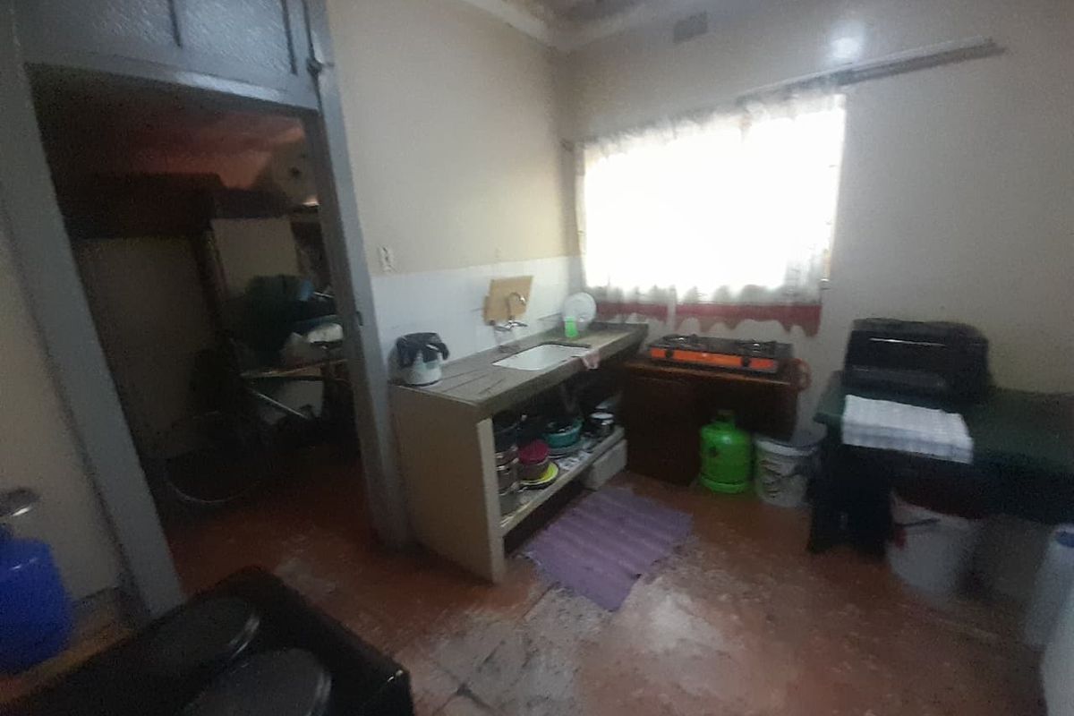 A basic kitchen area featuring a concrete counter, sink, and tiled splashback, requiring significant cosmetic updates and floor repairs.