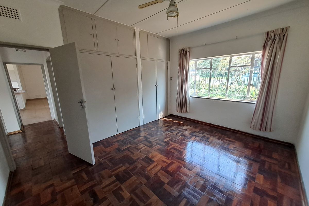 A spacious bedroom featuring original parquet flooring, built-in cupboards with overhead storage, and a ceiling fan, offering a blank canvas for renovation.