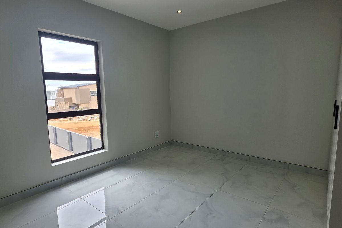 A bright, empty bedroom featuring modern tiled flooring, neutral walls, and a built-in cupboard, offering a clean canvas for personalization.