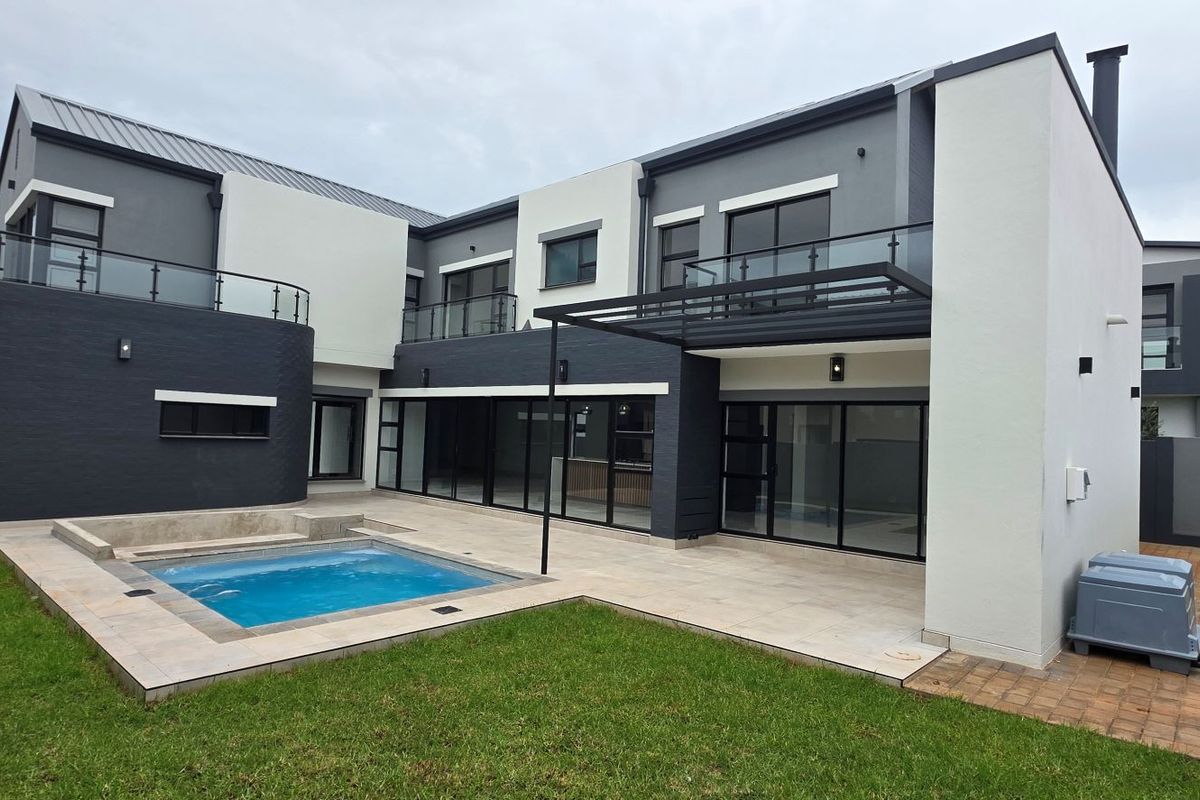 Modern double-story rear elevation featuring a swimming pool, tiled patio area, glass balcony balustrades, and large sliding glass doors.