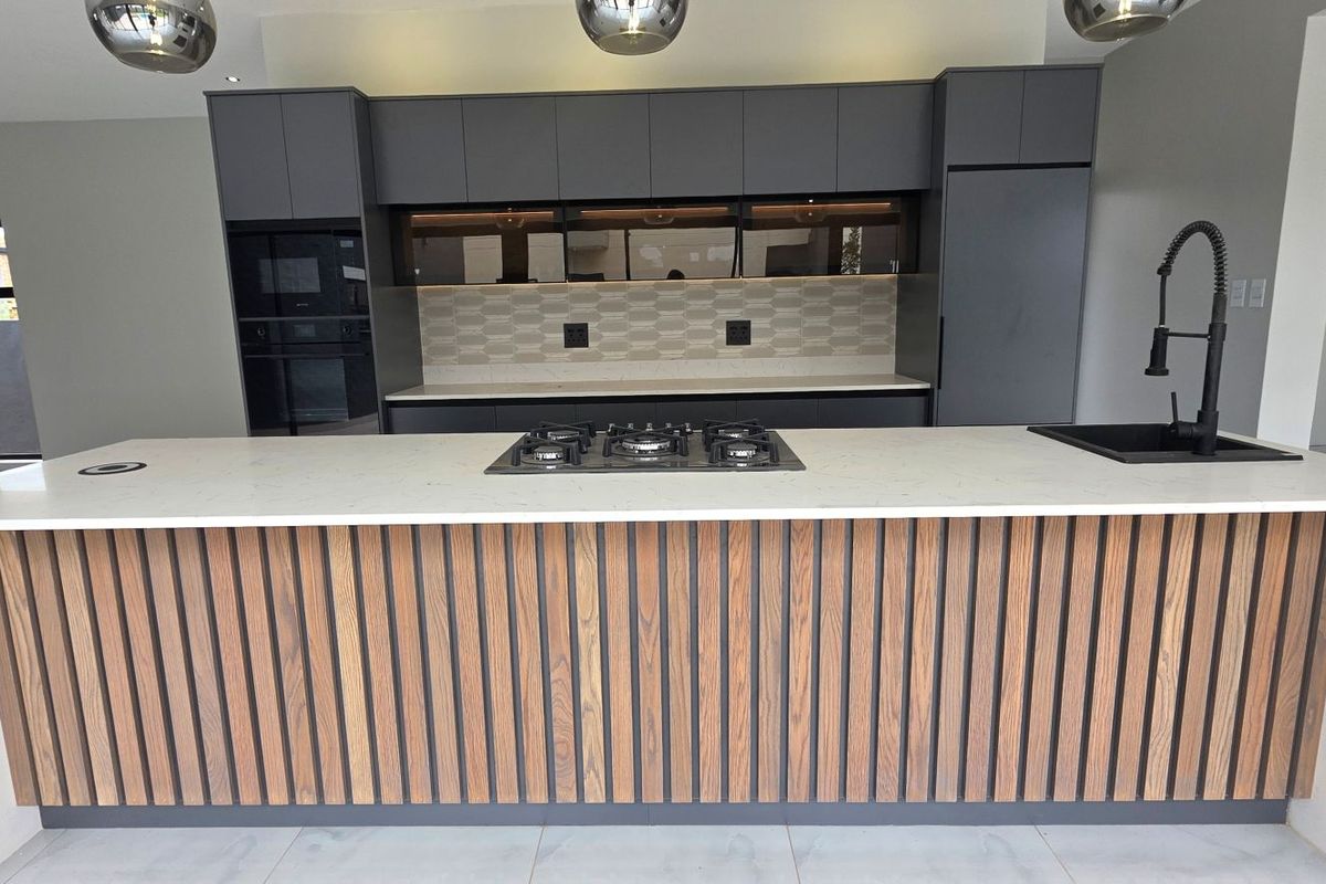 Modern kitchen featuring a large island with a gas hob, stone countertops, sleek dark cabinetry, and high-end finishes in an open-plan layout.