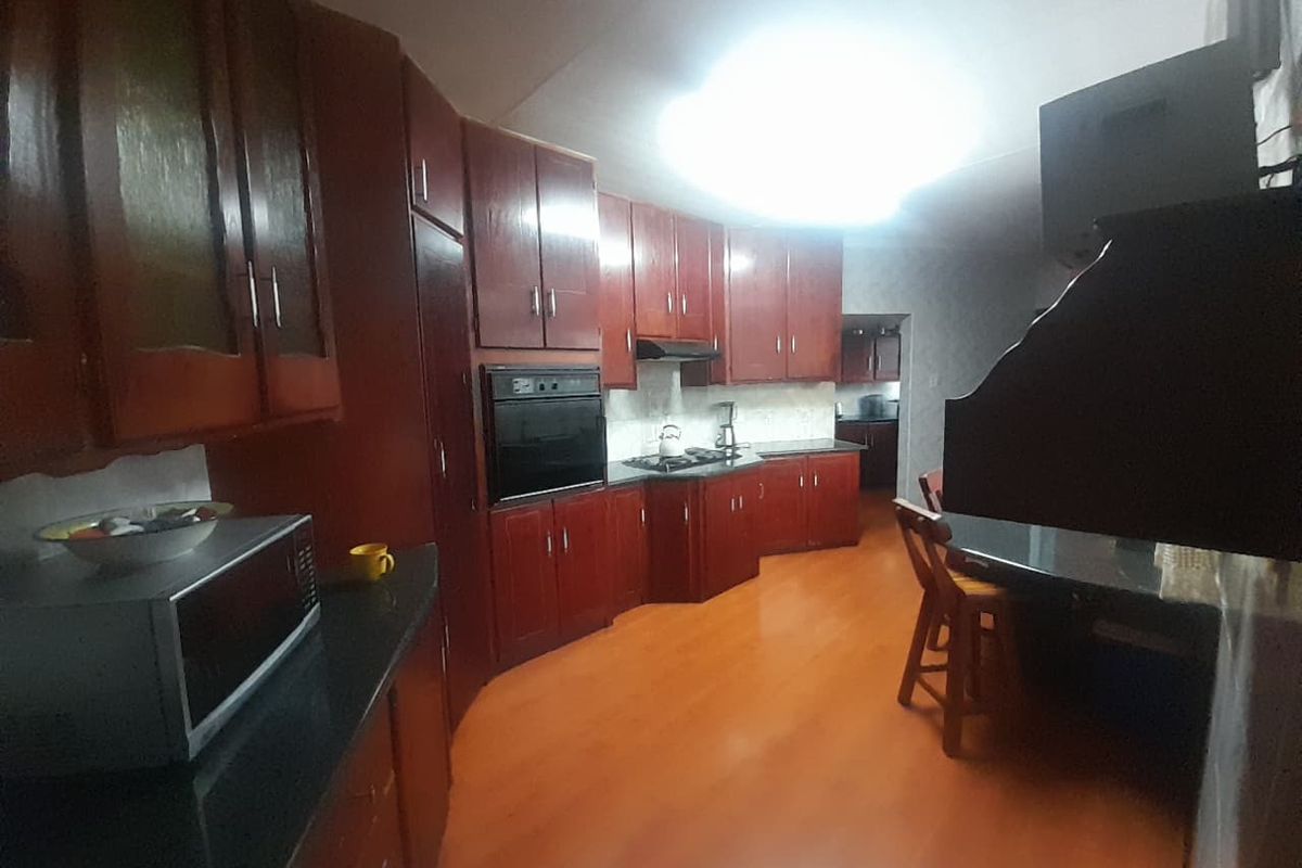 A spacious kitchen featuring extensive dark wood cabinetry, integrated oven, gas hob, and stone countertops, offering a functional layout with potential for modernization.