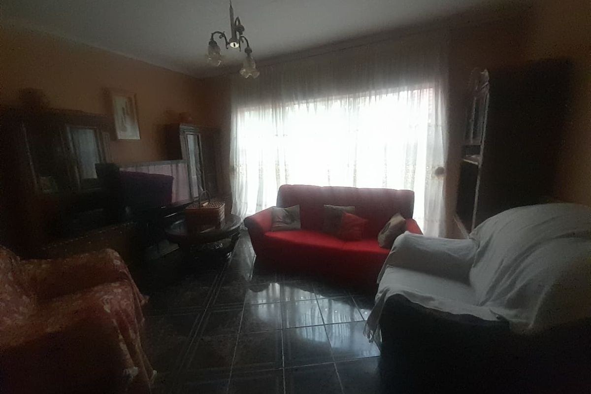 A dimly lit living room featuring dark tiled flooring and a large window, offering a dated interior space ready for modernization.