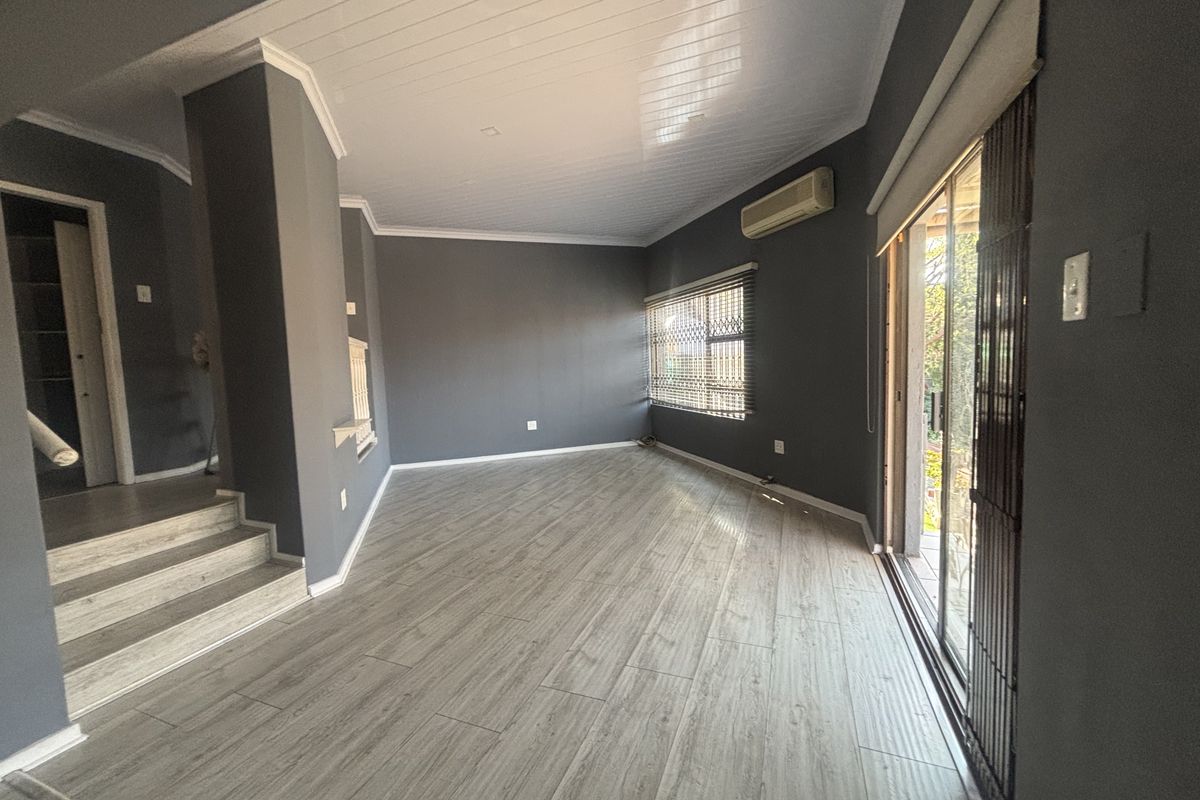 Spacious, empty living area featuring modern laminate flooring, a split-system air conditioner, and sliding glass doors leading to the exterior.