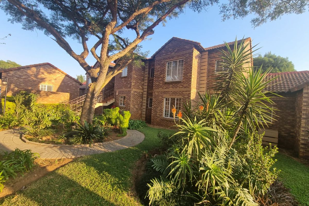 A well-maintained townhouse exterior featuring a classic face brick facade, tiled roof, and a lush, landscaped garden with a paved walkway.