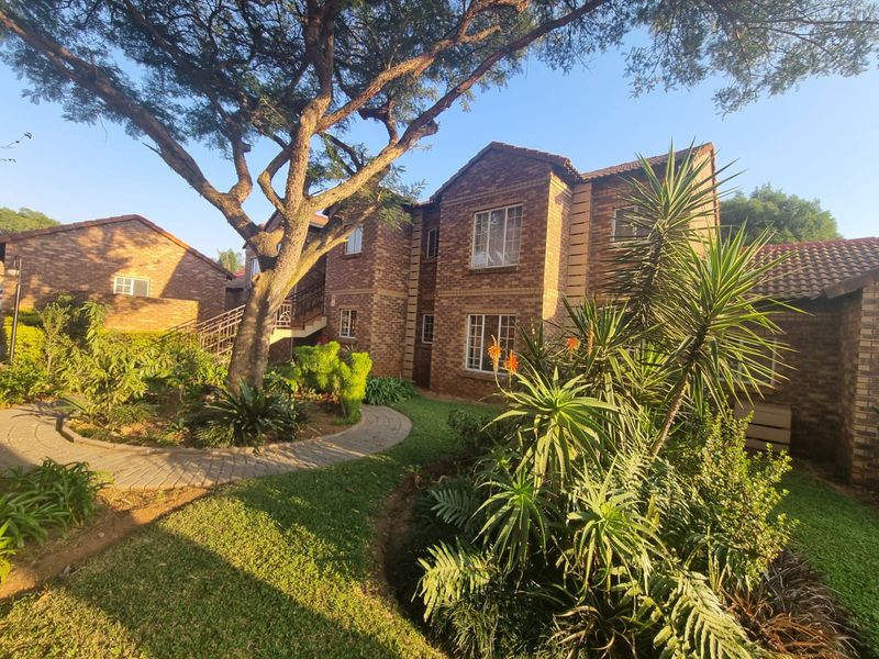 A well-maintained townhouse exterior featuring a classic face brick facade, tiled roof, and a lush, landscaped garden with a paved walkway.