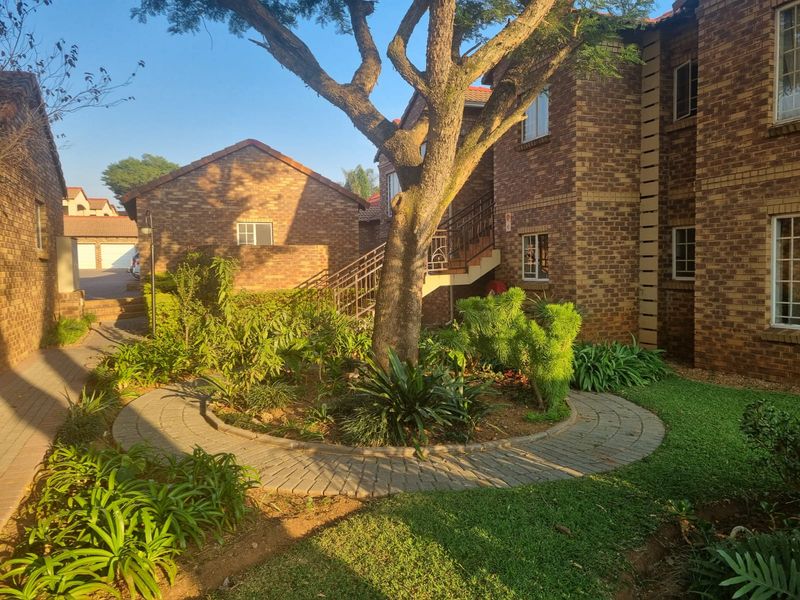 A well-maintained townhouse complex exterior featuring face brick construction, a central landscaped garden with a paved walkway, and an external staircase.