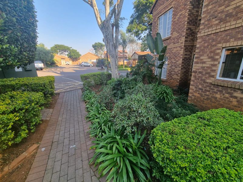 A view of the townhouse front exterior featuring a brick facade, a paved walkway, and established garden landscaping.