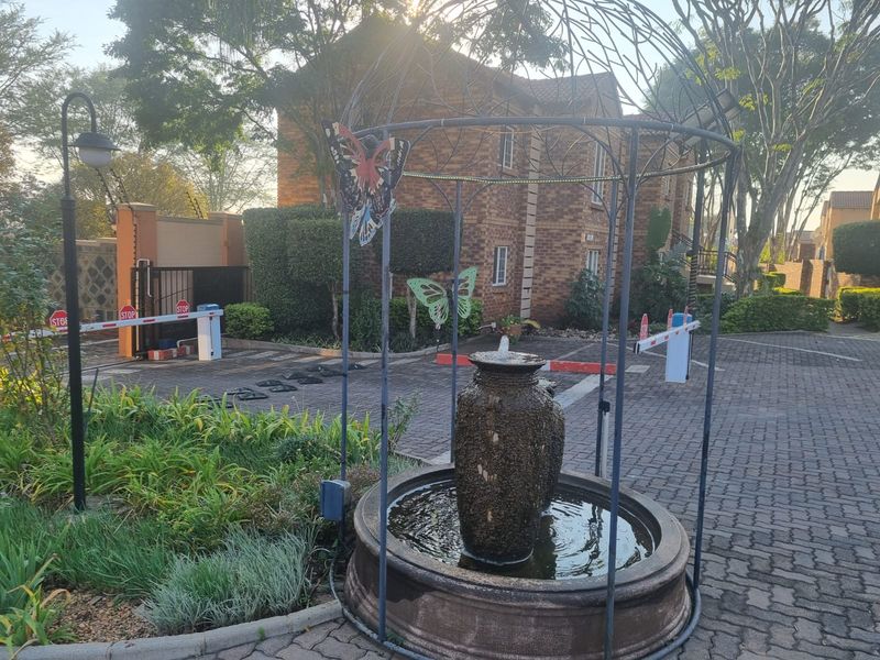 Front entrance area of the townhouse complex featuring a security boom gate, brick paved driveway, and a decorative water fountain.