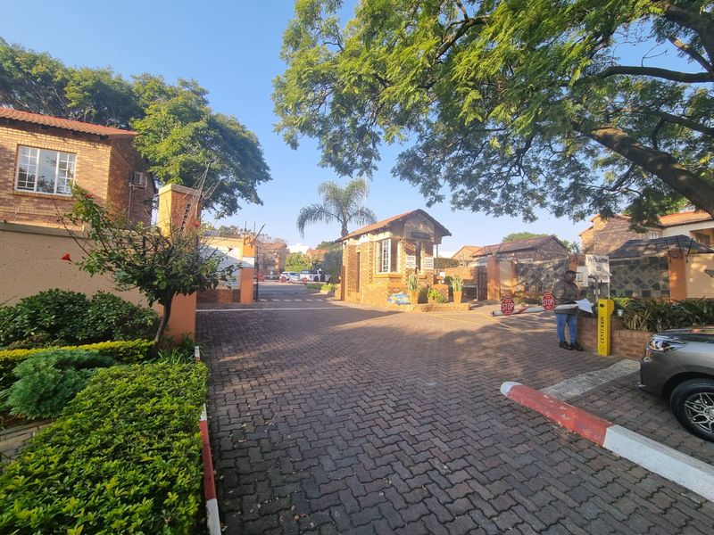 The entrance to the townhouse complex features a secure gatehouse, brick-paved driveway, and controlled boom gate access.