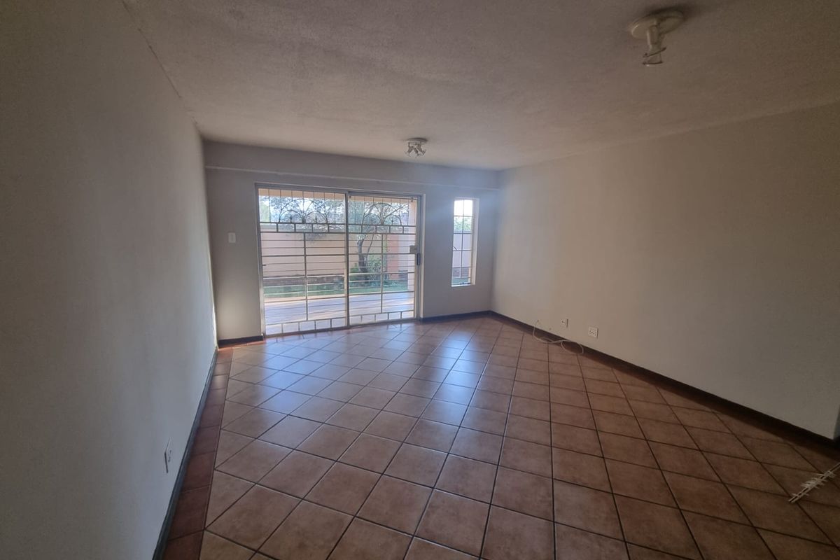 An empty living room featuring tiled flooring, a sliding glass door with security gate, and access to an outdoor area.