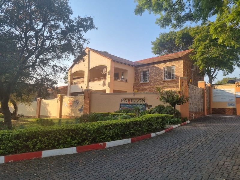 Front exterior view of the Papillon townhouse complex, featuring brick facade architecture, a paved driveway, and secure boundary wall with electric fencing.