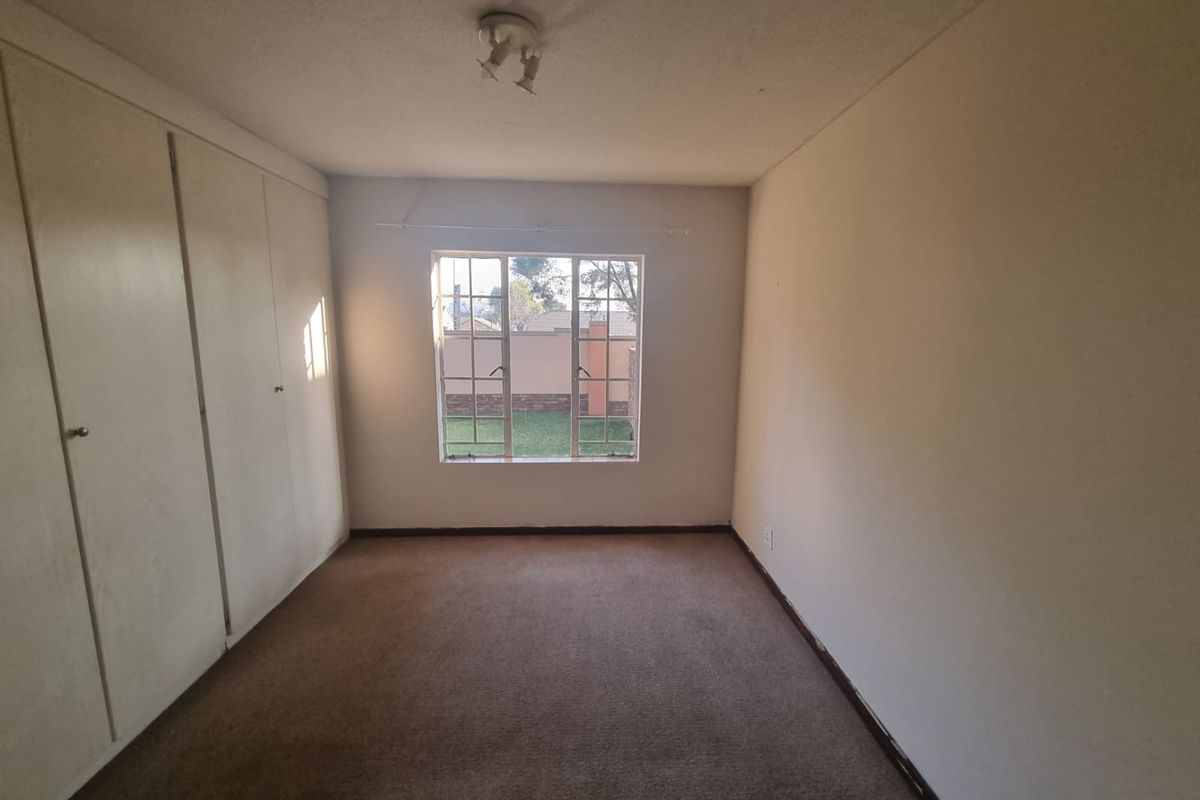 An empty bedroom featuring built-in cupboards, carpeted flooring, and a window overlooking the garden area.