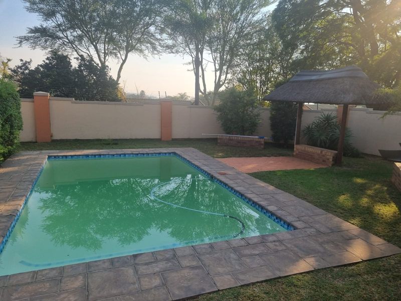 Private backyard featuring a swimming pool with paved surround and a traditional thatched lapa, enclosed by a perimeter wall.