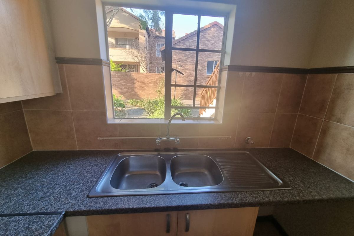 A functional kitchen area featuring a double bowl stainless steel sink, laminate countertops, and tiled splashback, with a window overlooking the exterior.