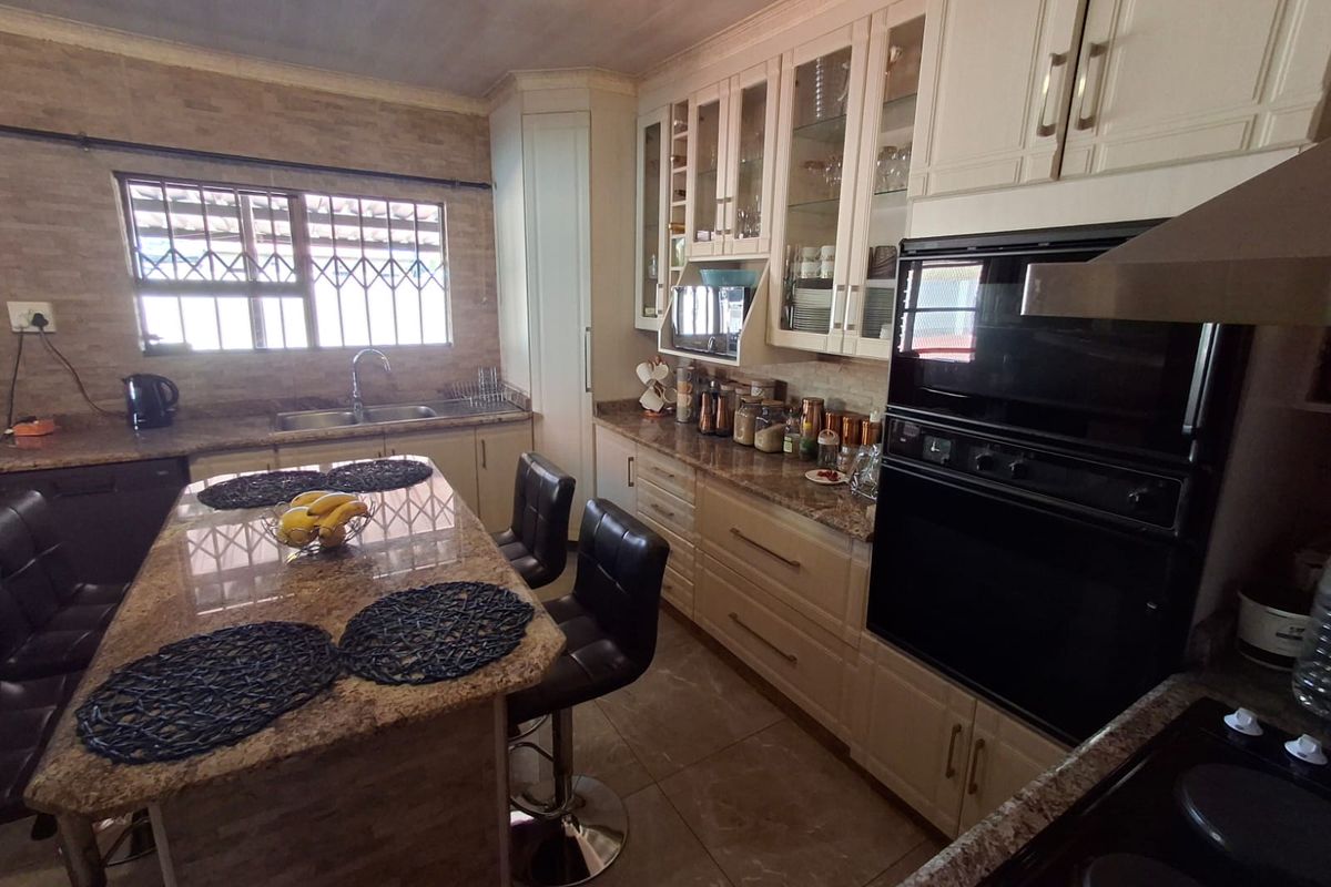 A functional kitchen featuring granite countertops, a central island, built-in oven, extractor fan, and ample cabinetry with glass-fronted display units.