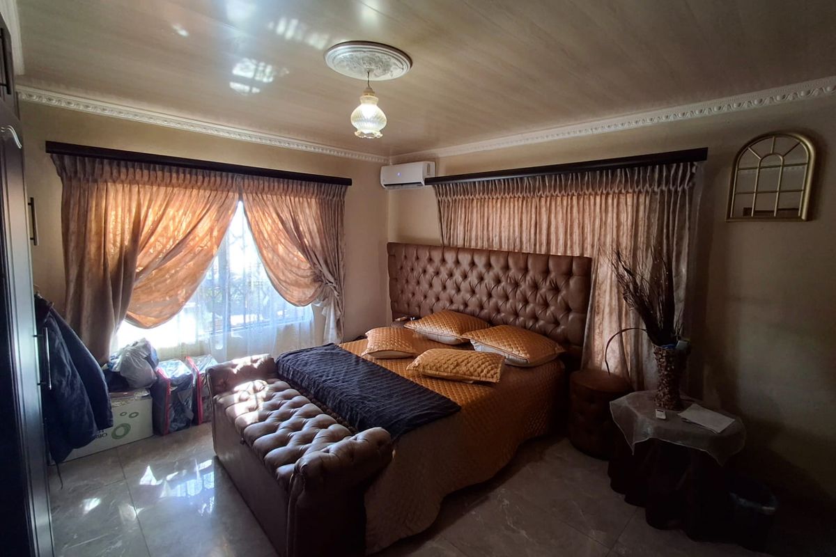 A well-maintained bedroom featuring tiled flooring, decorative coving, a ceiling rose, and a wall-mounted split-system air conditioner.