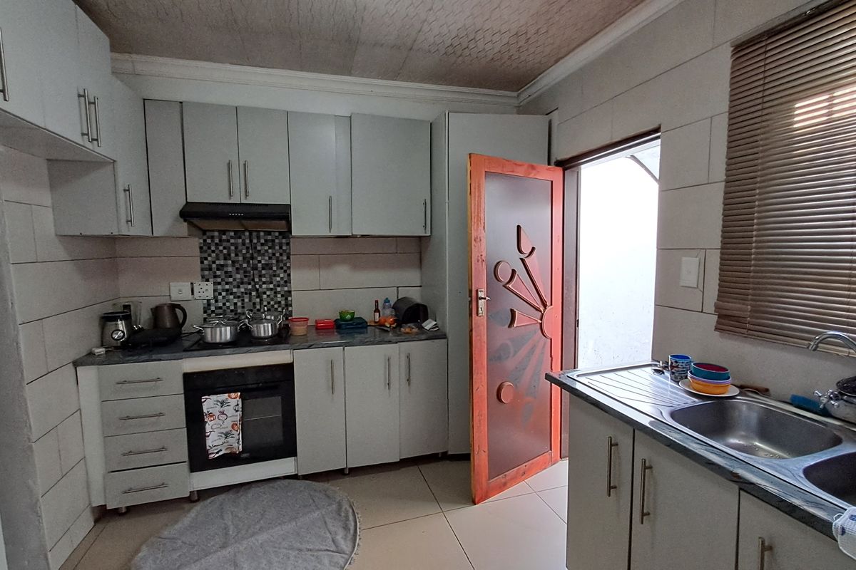 Functional kitchen featuring built-in cabinetry, integrated oven and hob, tiled splashbacks, and a double sink with direct access to the exterior.