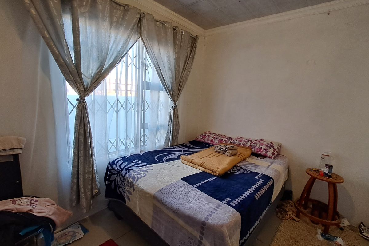 A compact bedroom featuring tiled flooring, a security gate on the window, and ceiling detailing, offering a functional space for rest.
