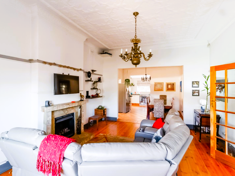 Spacious open-plan living area featuring polished timber floors, an ornate ceiling, a fireplace with stone hearth, and a classic chandelier.