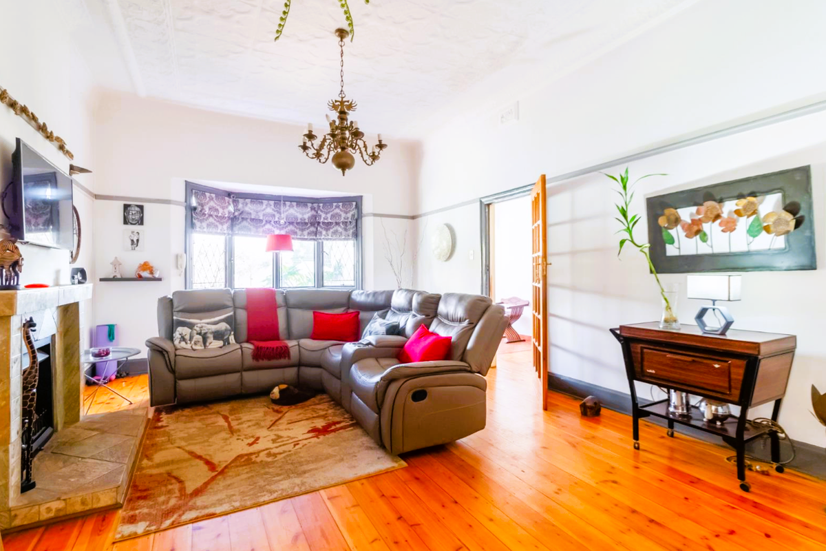 A bright living room featuring polished timber flooring, an ornate ceiling, a fireplace with a stone hearth, and a classic bay window.