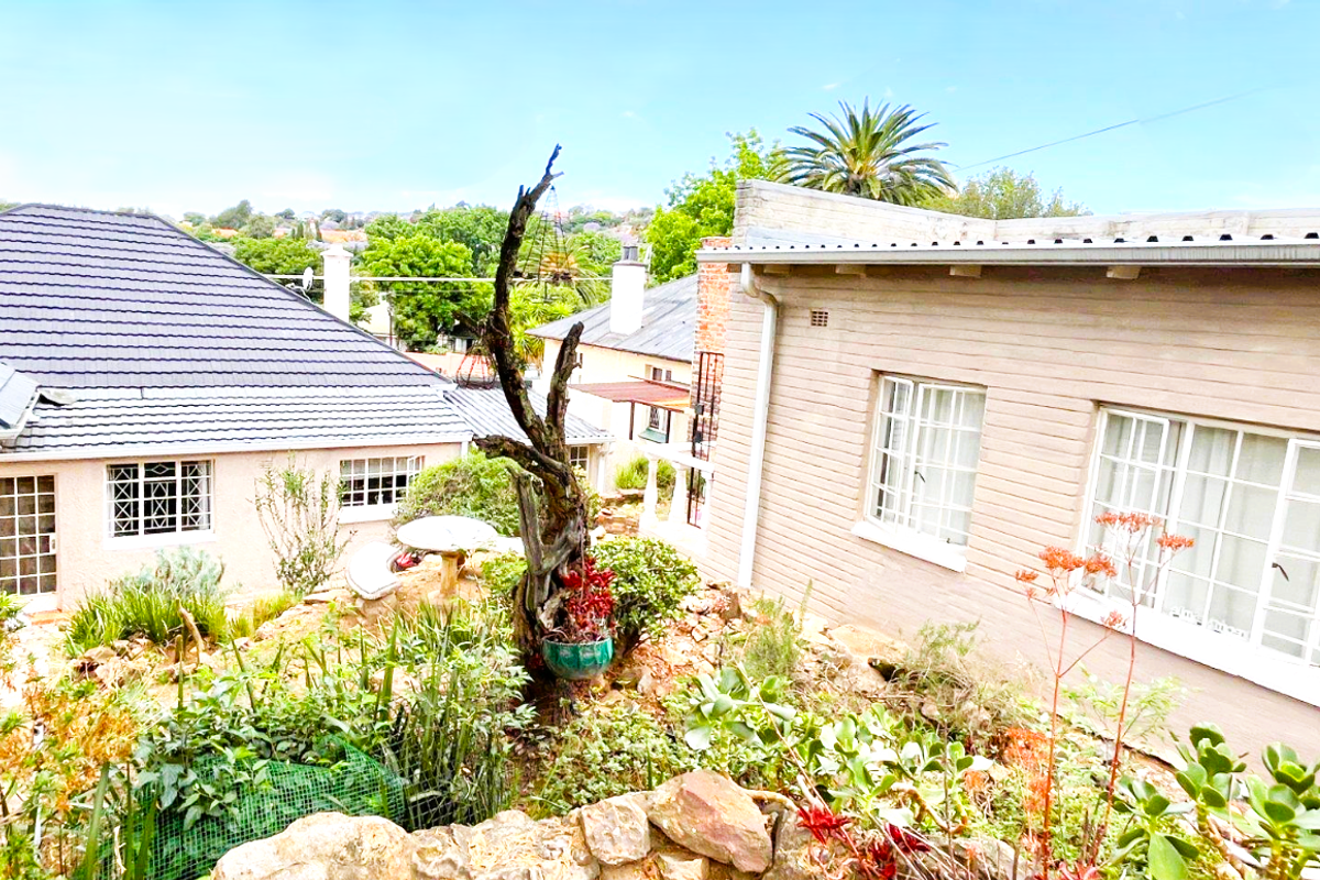 Rear view of the property showing the garden area, stone retaining wall, and exterior facades of the house with tiled roofing.