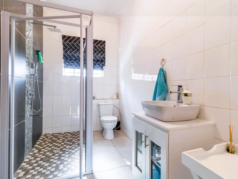 Modern bathroom featuring a glass-enclosed shower with mosaic accents, a vessel sink vanity, and white wall tiling.