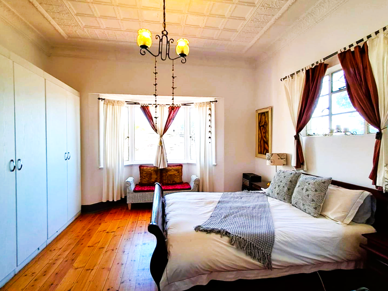 Spacious bedroom featuring original timber flooring, a decorative pressed metal ceiling, built-in wardrobes, and a charming bay window.