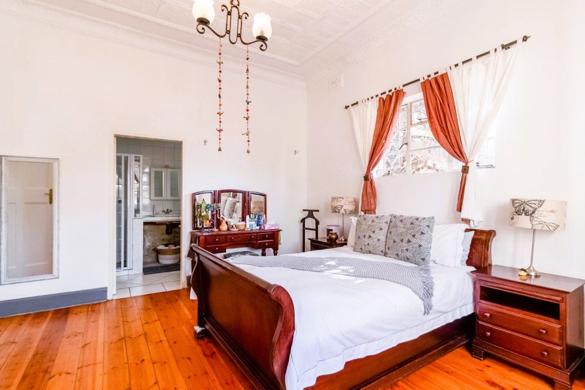 Spacious bedroom featuring original timber flooring, high ceilings with ornate detailing, and direct access to an adjoining en-suite bathroom.