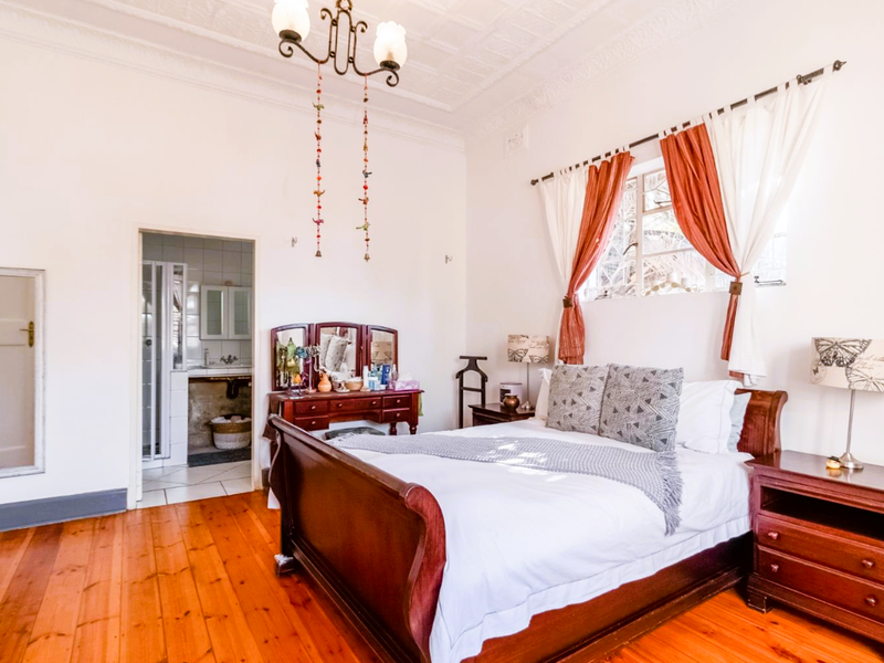 Spacious bedroom featuring original timber flooring, high ceilings with ornate detailing, and direct access to an adjoining en-suite bathroom.