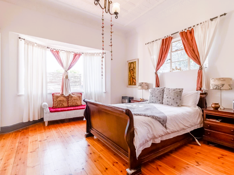 A bright bedroom featuring polished timber flooring, a classic bay window, and a decorative ceiling, offering a warm and inviting atmosphere.